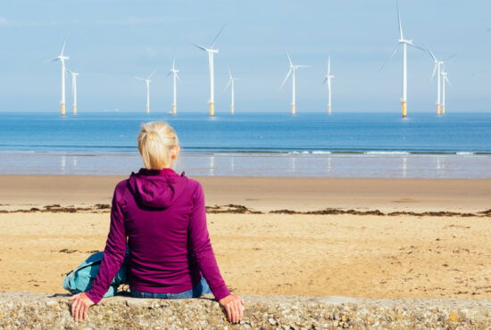 Woman observing an offshore windfarm at Redcar in the northeast of England.