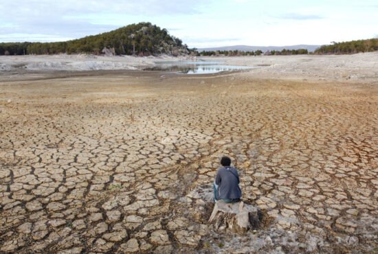 Young man sitting helplessly in a pond drained by drought